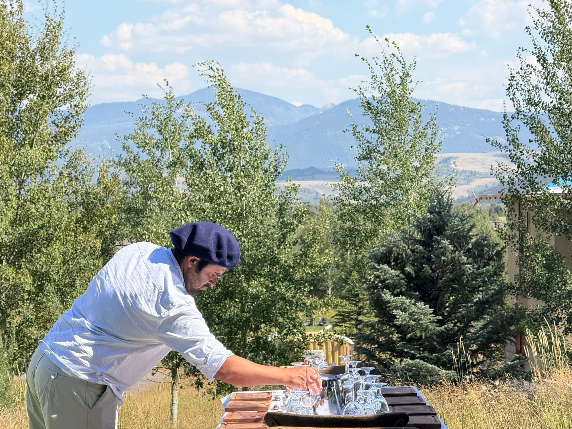Pancho arranging glassware on a table outdoors with a mountain range in the distance